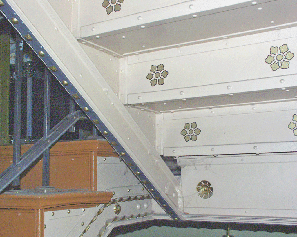Detail einer restaurierten, gusseisernen Treppe mit vergoldeten Zierornamenten.